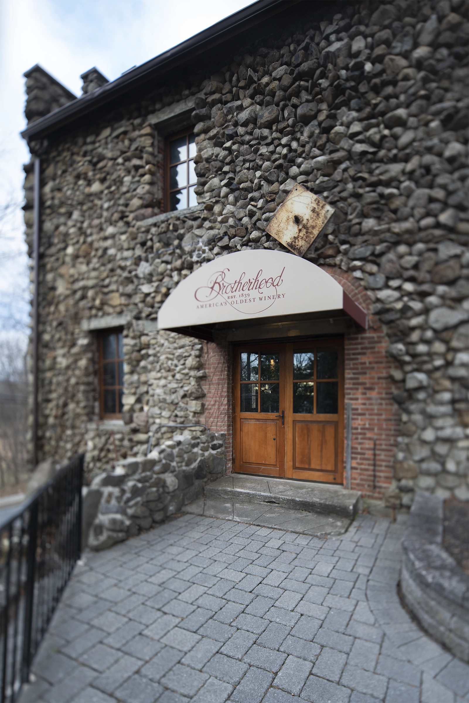 Grand Salon entrance with cream awning and wooden doors in a brick arch, fieldstone wall.