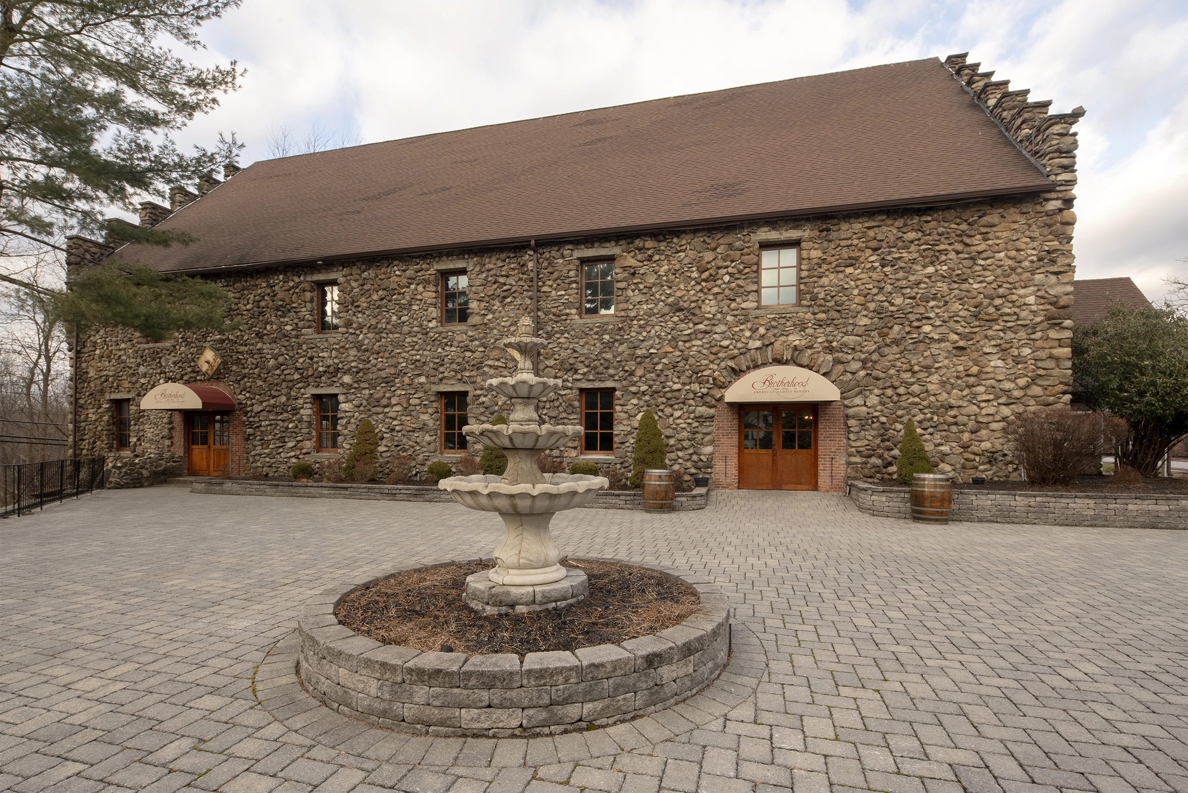 Front courtyard of the fieldstone Grand Salon, with a circular tiered fountain in the foreground and the building in the background.