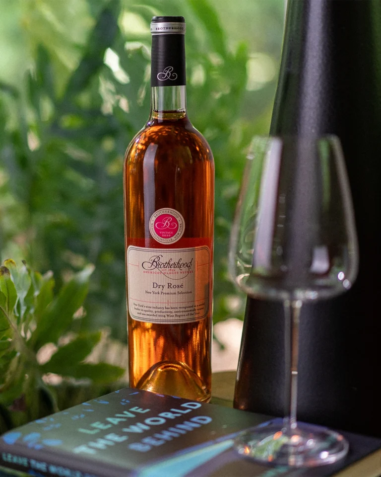 Dry rosé wine bottle surrounded by greenery with tasting glass