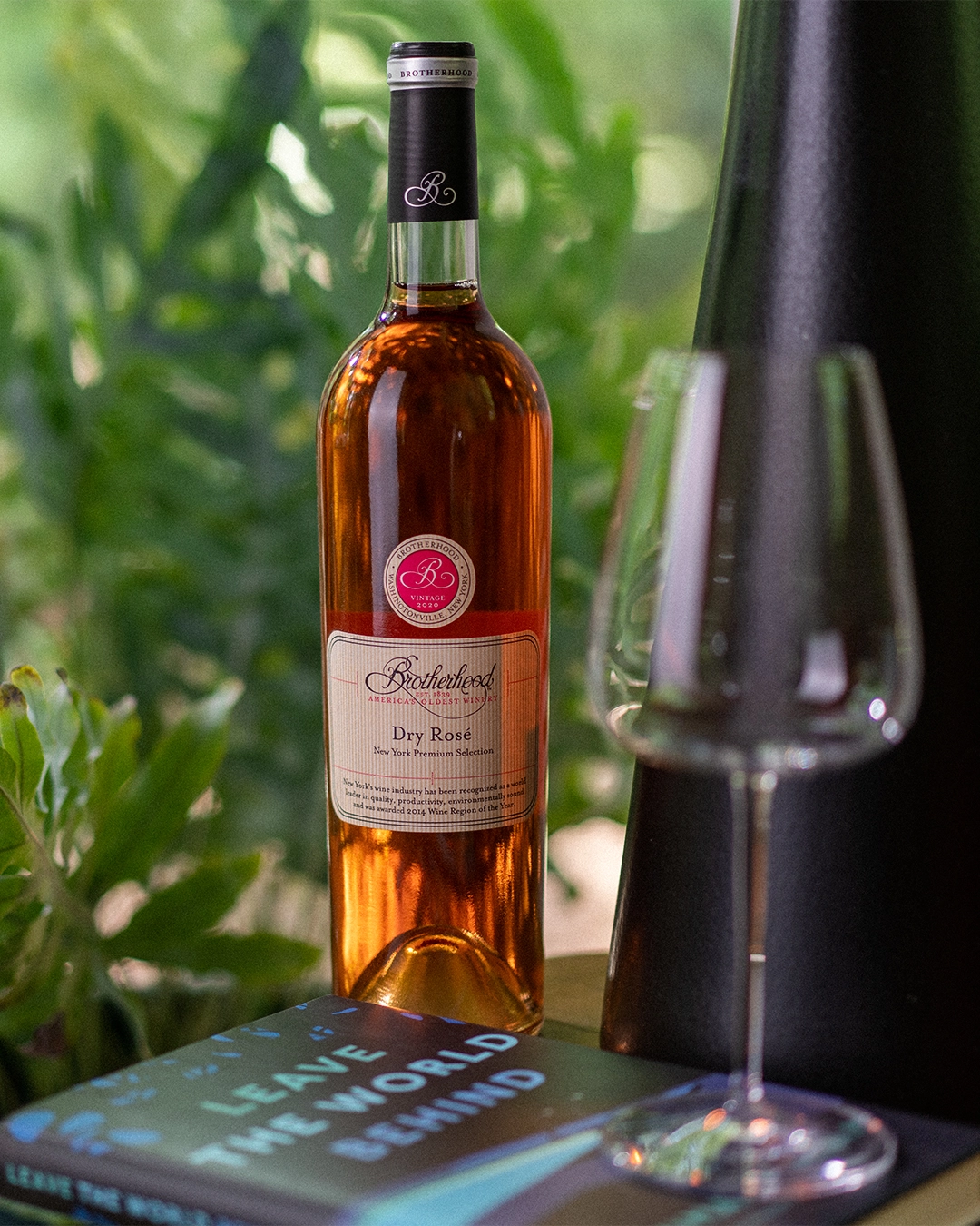 Dry rosé wine bottle surrounded by greenery with tasting glass
